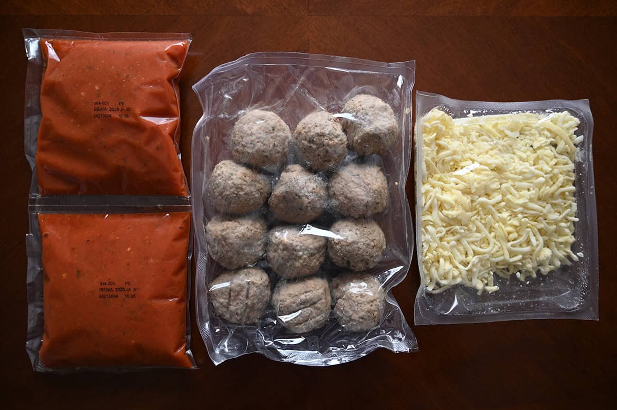 Image of two packets of sauce, a package of meatballs and a package of cheese sitting on a table.