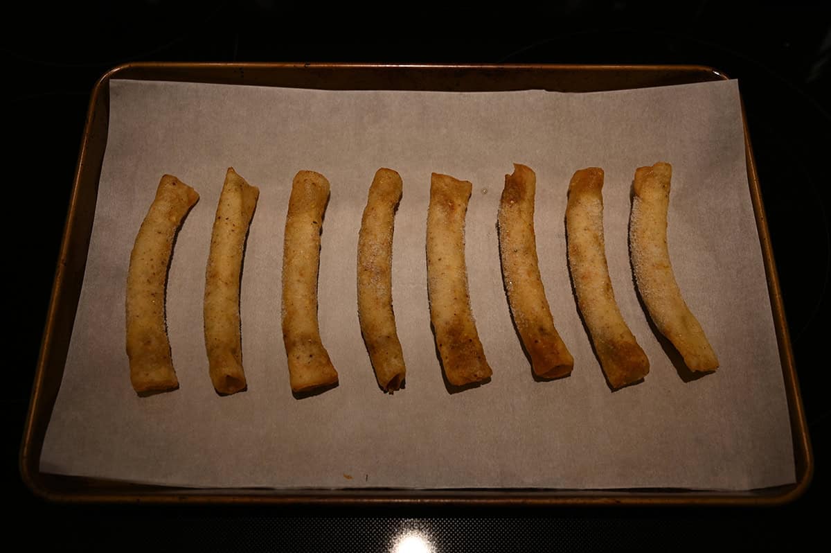 Image of eight rolled tacos on a parchment paper lined baking sheet ready to be baked.