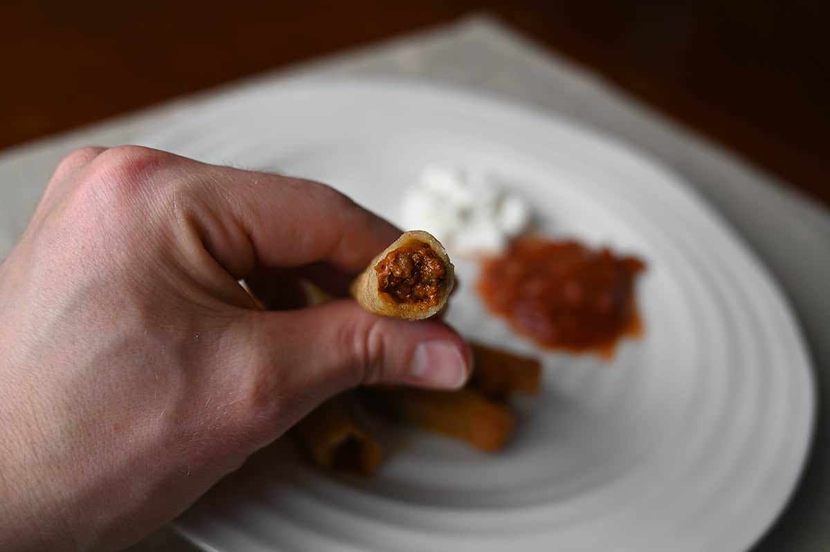 Image of a hand holding one rolled taco close to the camera with a bite taken off so you can see the filling.