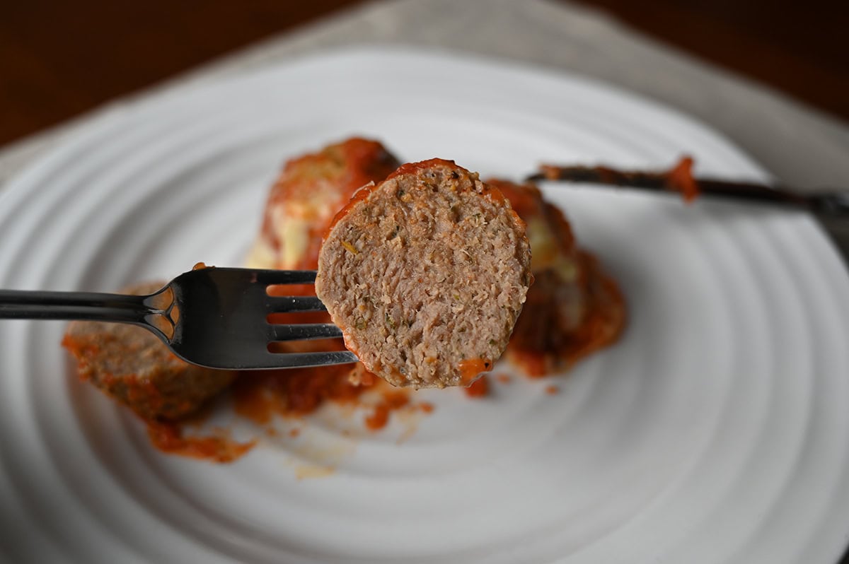 Image of a fork with a meatball cut in half hovering over a plate of meatballs.