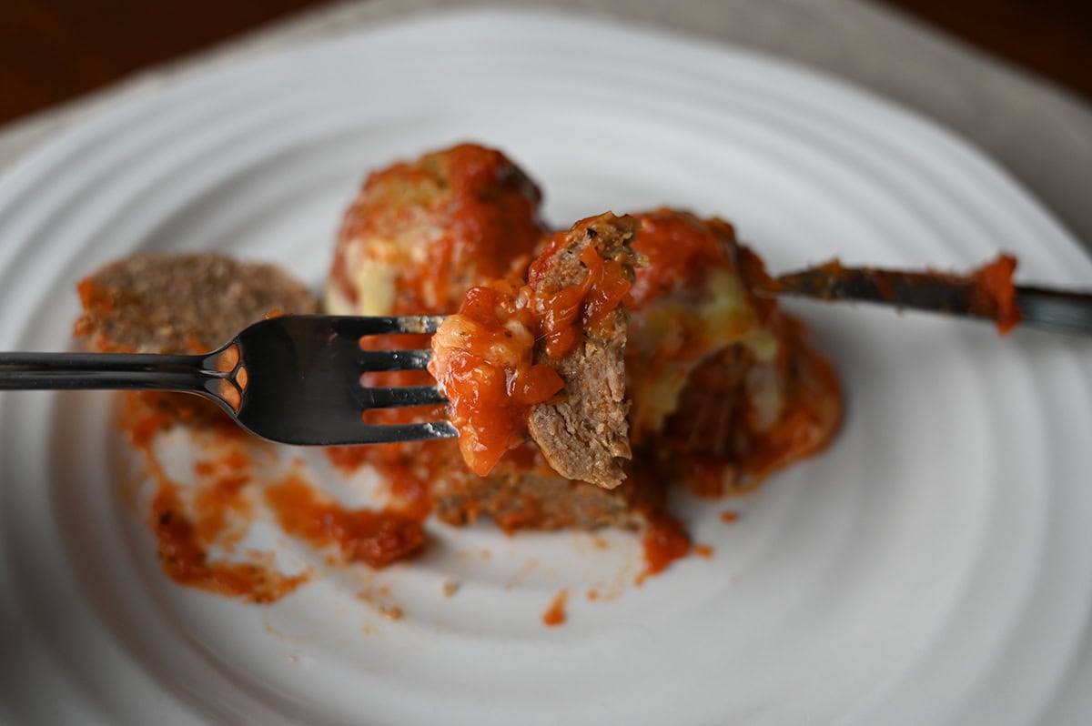 Closeup image of a fork with a piece of meatball in it with the plate of meatballs in the background.