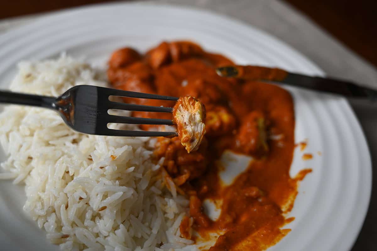 Image of a fork with a piece of chicken and curry on it hovering over a plate of curry and rice.