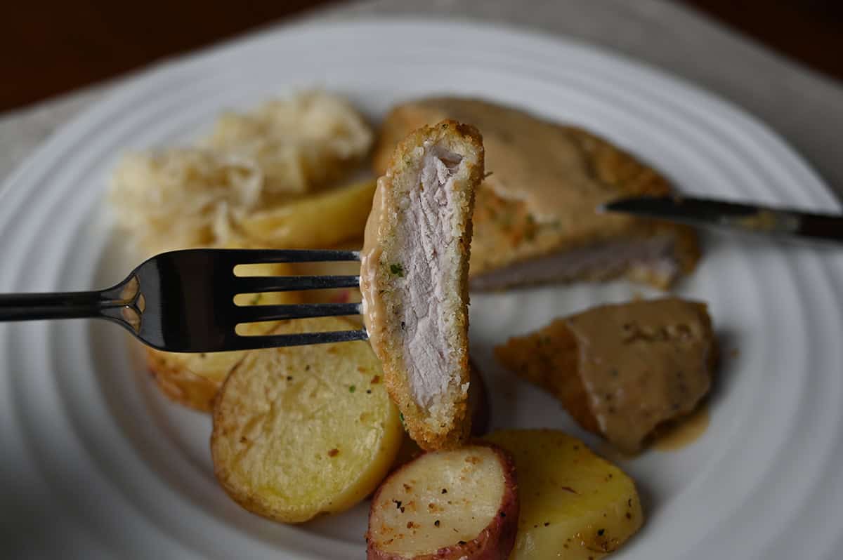 Image of a slice of pork schnitzel on a fork so you can see the inside of the pork cutlet.