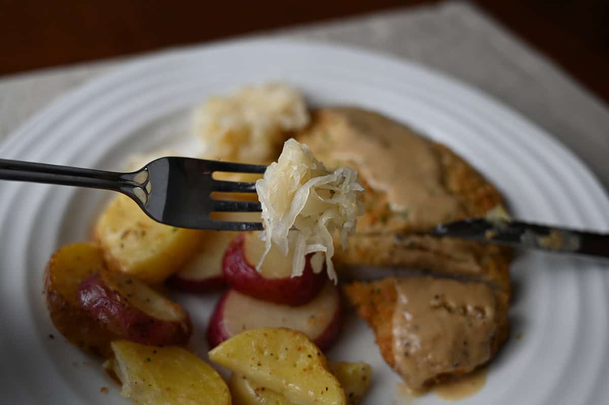 Closeup image of a fork hovering over a plate of pork schnitzel with sauerkraut on the fork.