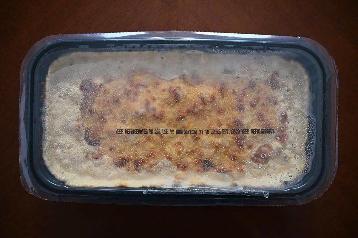 Top down image of a plastic container filled with bacon macaroni and cheese with a plastic seal on top. 