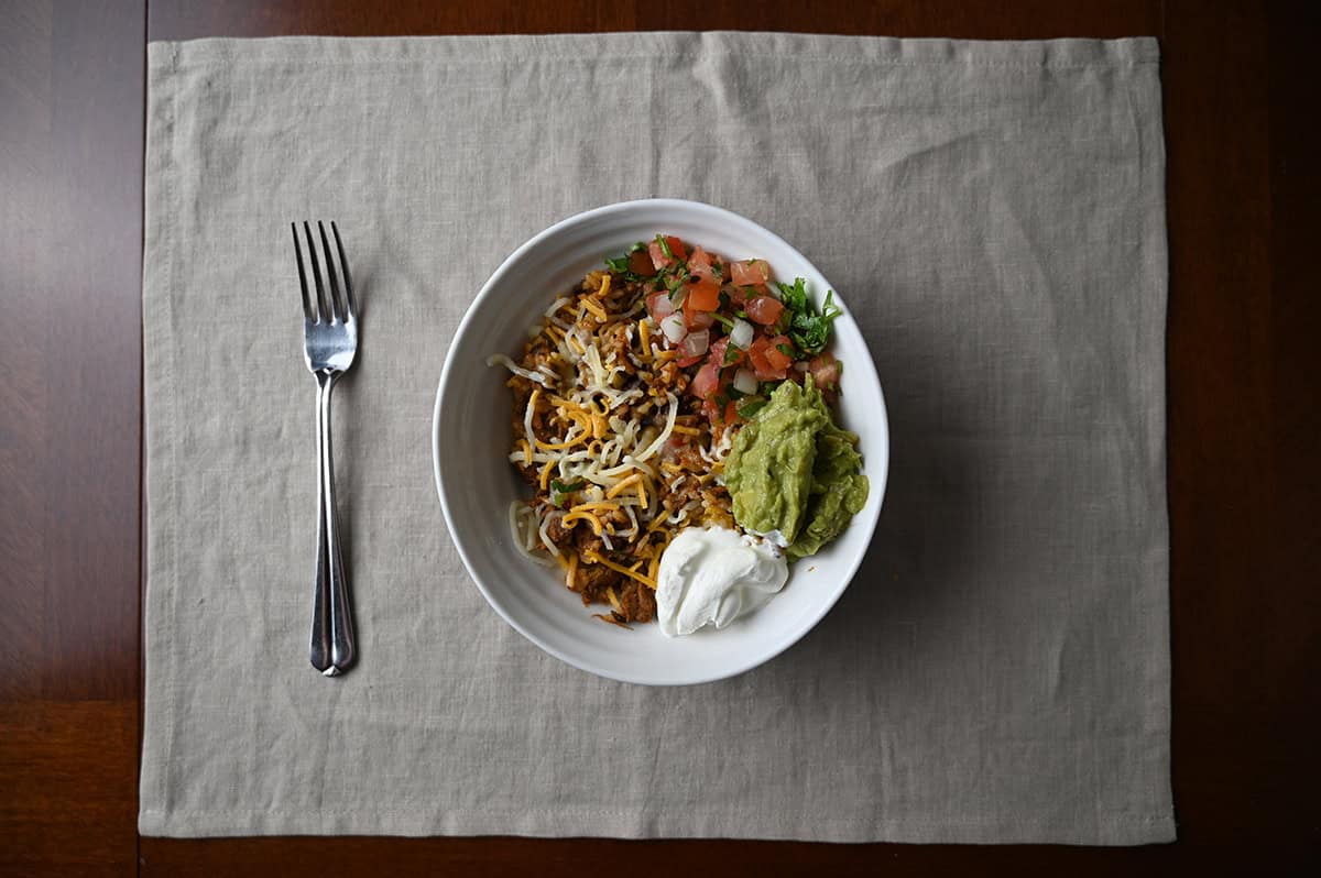 Top down image of a bowl of beef birria burrito mixture with sour cream, guacamole, pico de gallo and cheese on top.