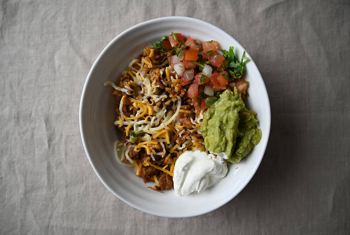 Closeup image of a beef birria burrito bowl with pico de gallo, sour cream, cheese and guacamole on it.