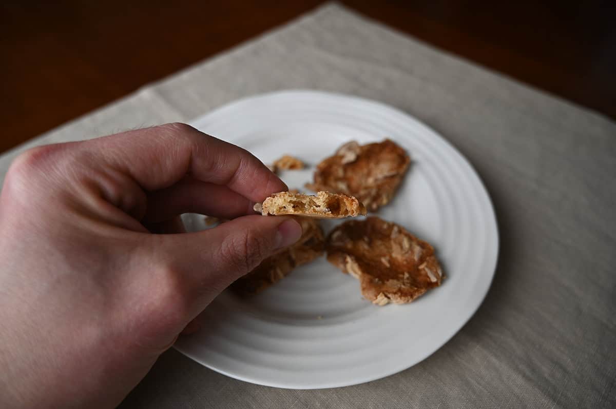 Image of a hand holding one almond crisp on it's side so you can see how thick it is.