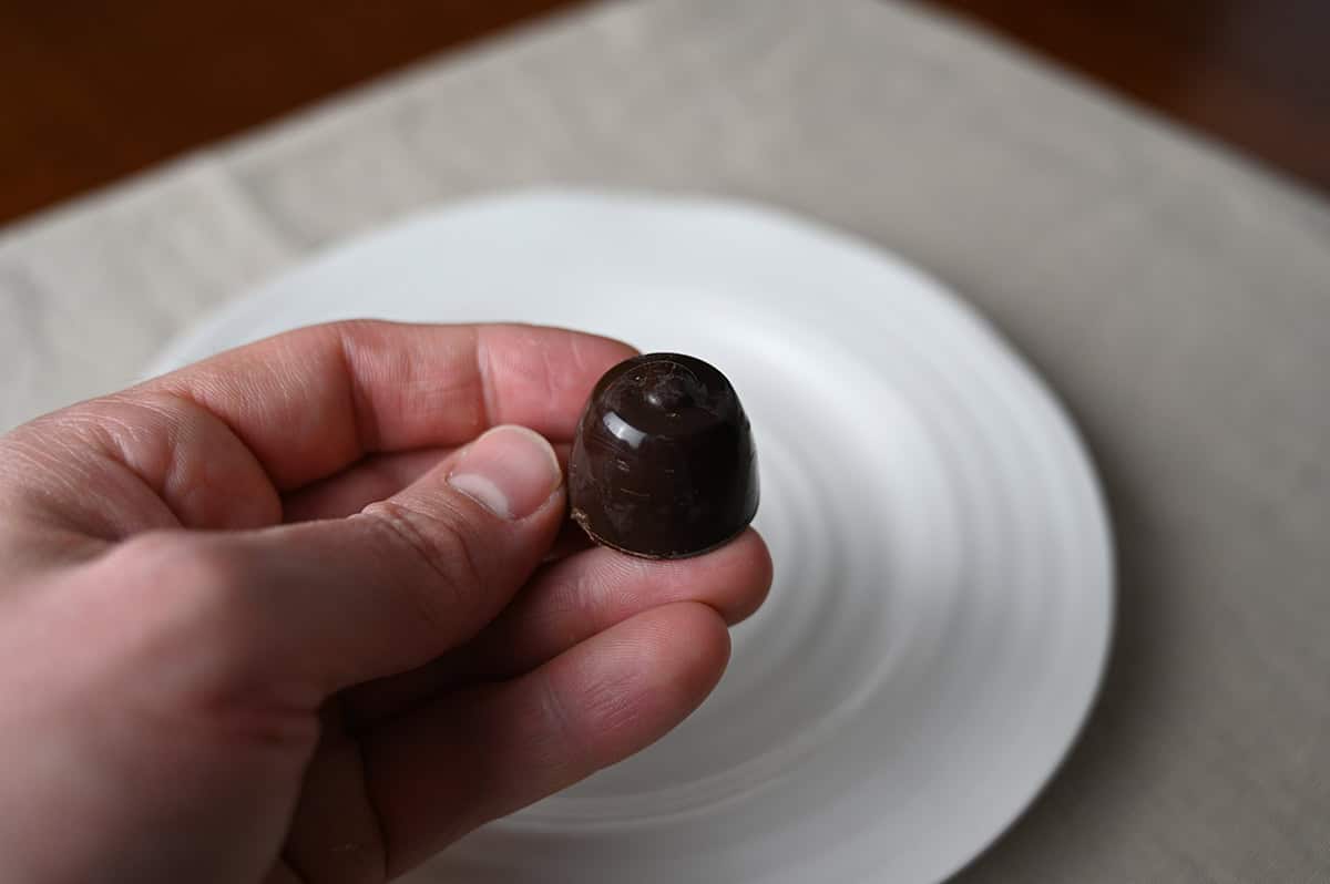 Image of a hand holding one Costco Zaini Boero Dark Chocolate Praline with Cherry in Alcohol unwrapped hovering over a white plate.