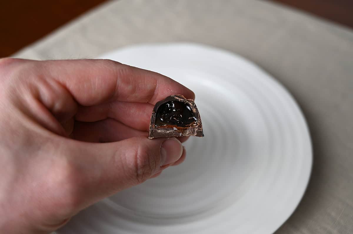 Image of a hand holding one chocolate with a bite taken out of it so you can see the cherry filling inside.