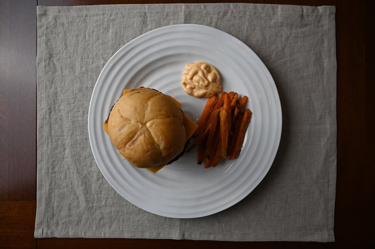 Image of white plate with a burger, sweet potato fires and aioli served on it.