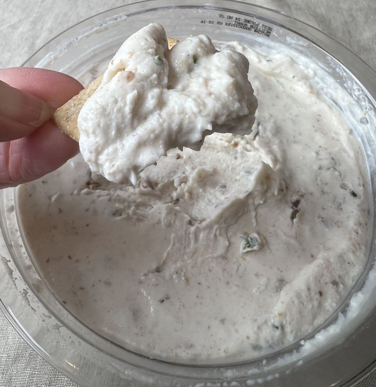 Image of a cracker with the dip on it hovering over the open container.