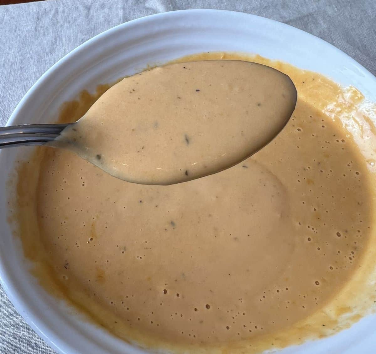 Image of a spoon with lobster bisque on it hovering over a bowl of lobster bisque.