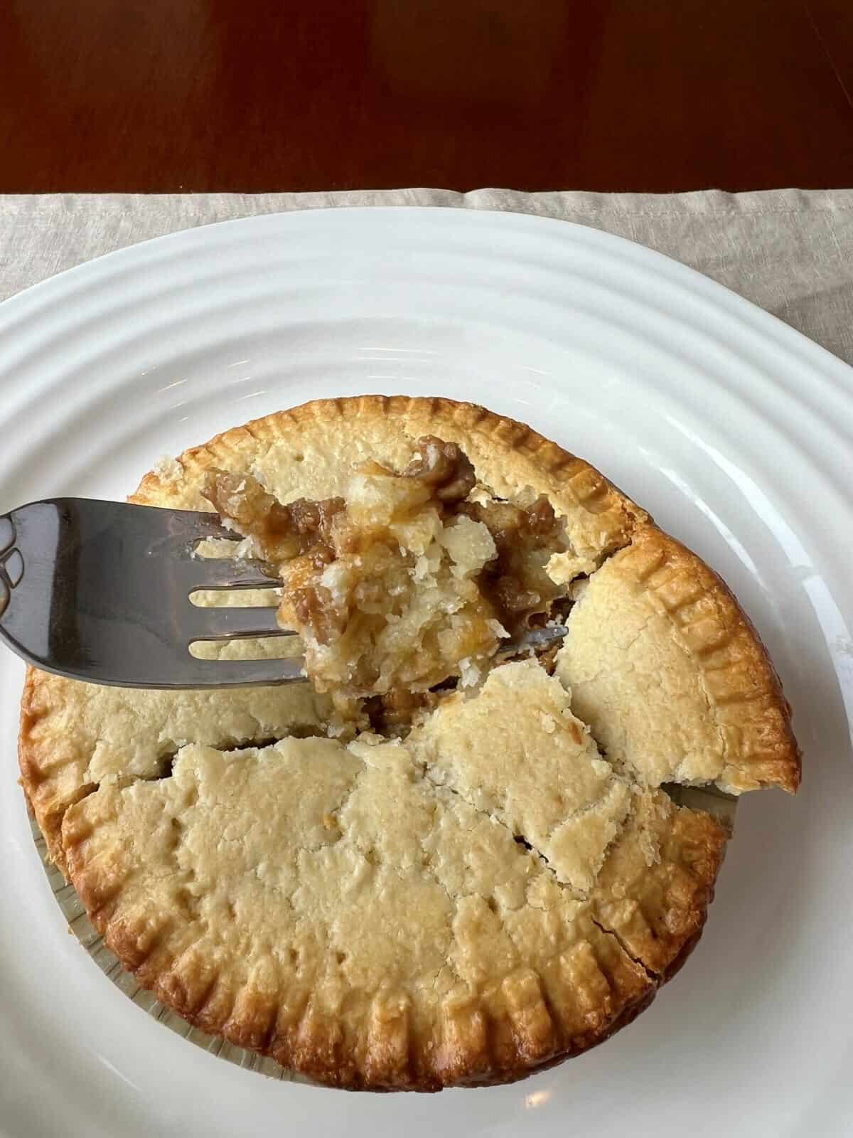 Image of a fork hovering over a meat pie with crust and meat pn the fork.