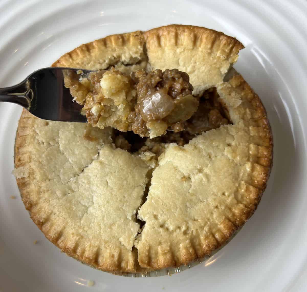 Image of a fork hovering over an open meat pie with ground beef, onions and potatoes on the fork.