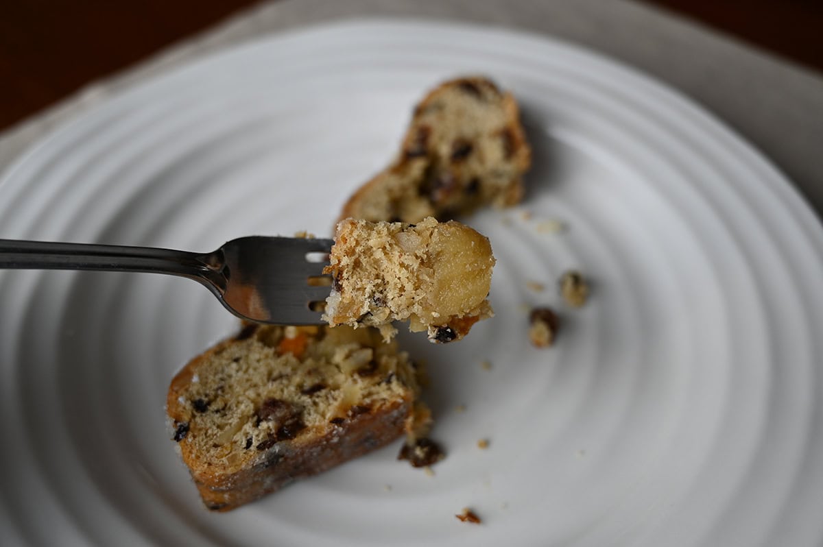 Image of a fork with a bite of Stollen on it with a slice of Stollen served on a white plate in the background. 