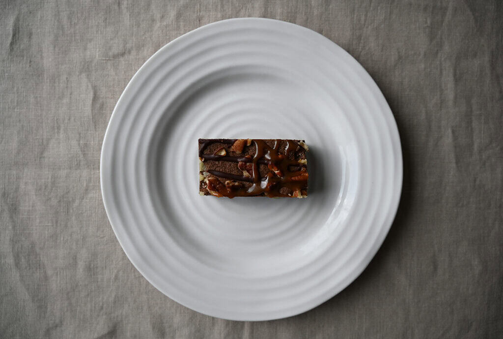 Image of a pecan caramel brownie served on a white plate.