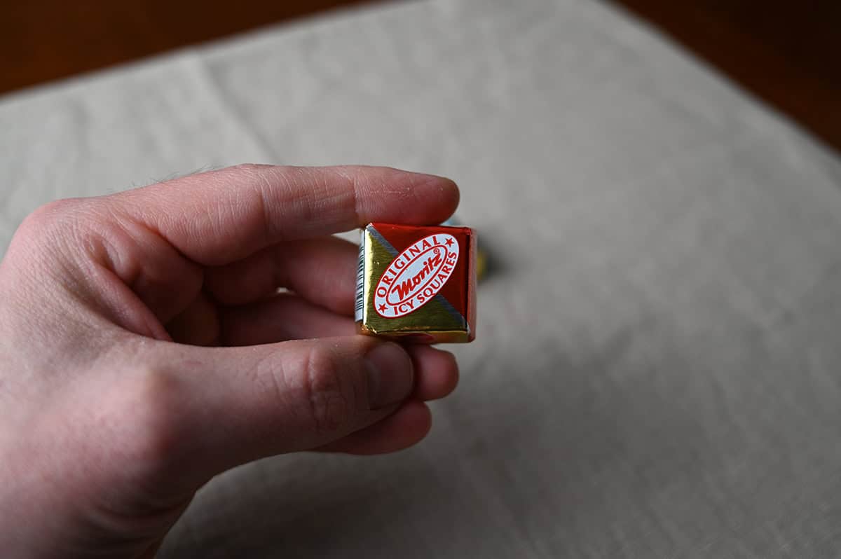 Image of a hand holding one single wrapped icy square instead of the camera.