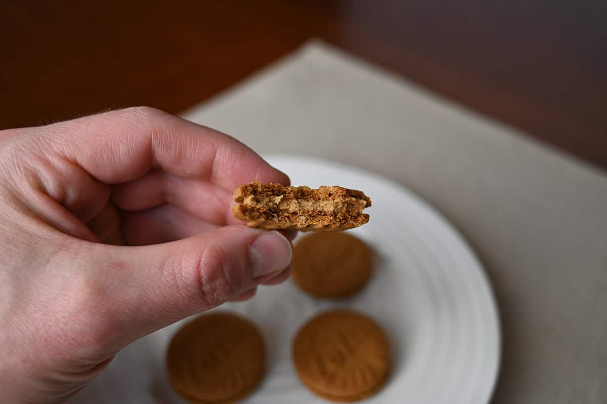 Image of a hand holding one sandwich cookie with a few bites taken out of it so you can see the center. 