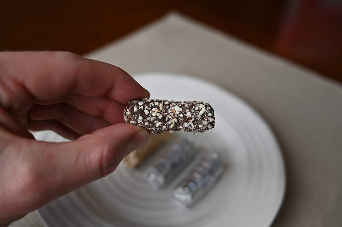 Image of a hand holding one unwrapped Almond Roca chocolate close to the camera so you can see the shape and size.