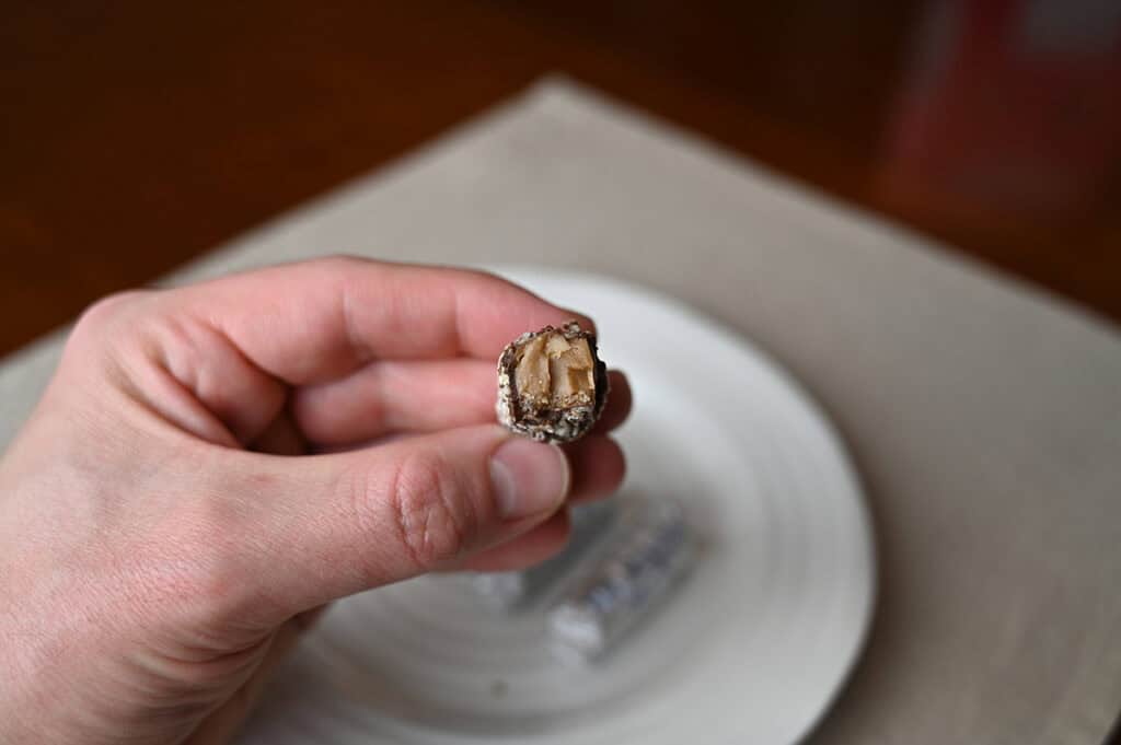 Image of a hand holding one Almond Roca chocolate close to the camera with a bite taken out of it so you can see the center.