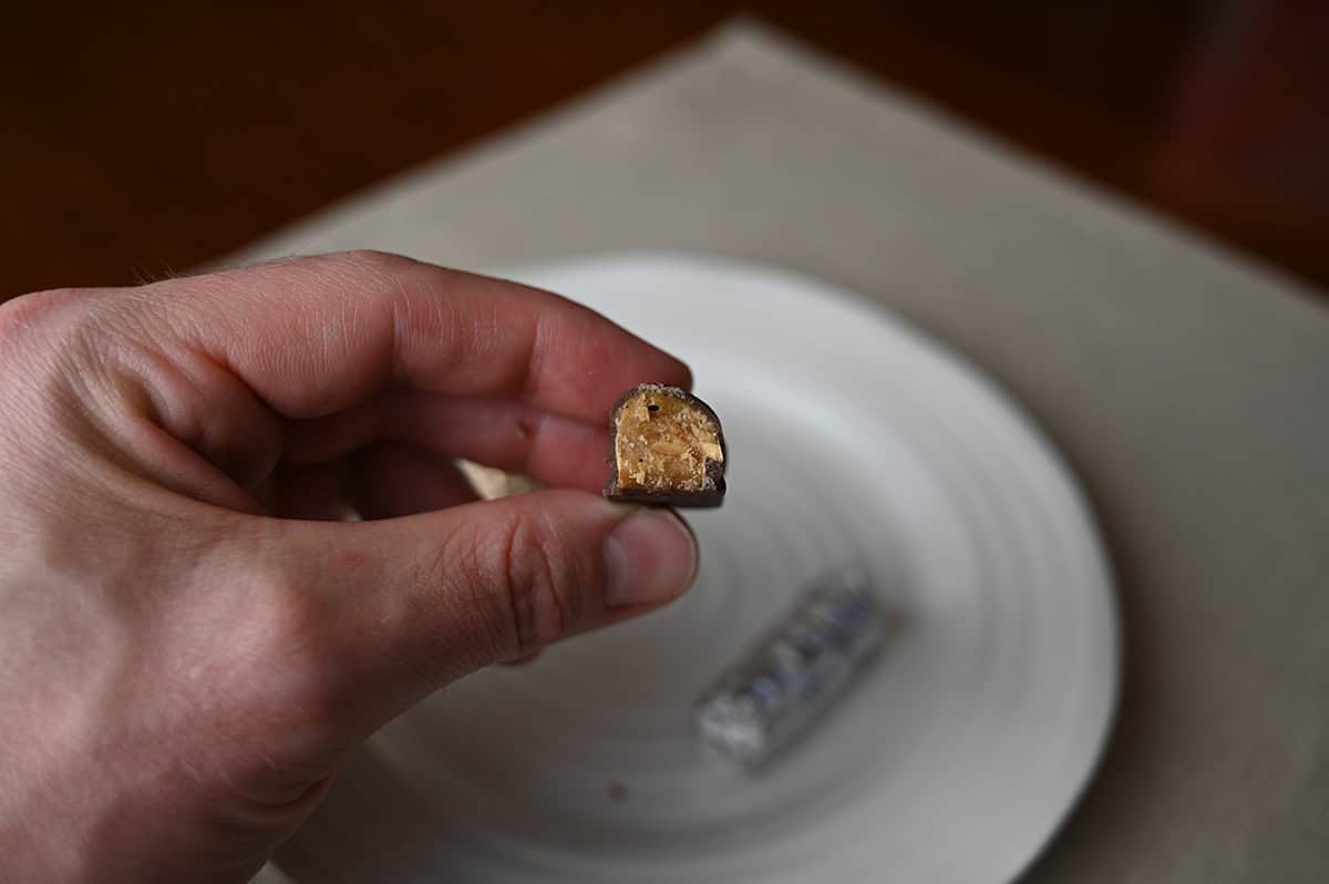 Image of a hand holding one Macadamia Roca with a bite taken out of it so you can see the center. 