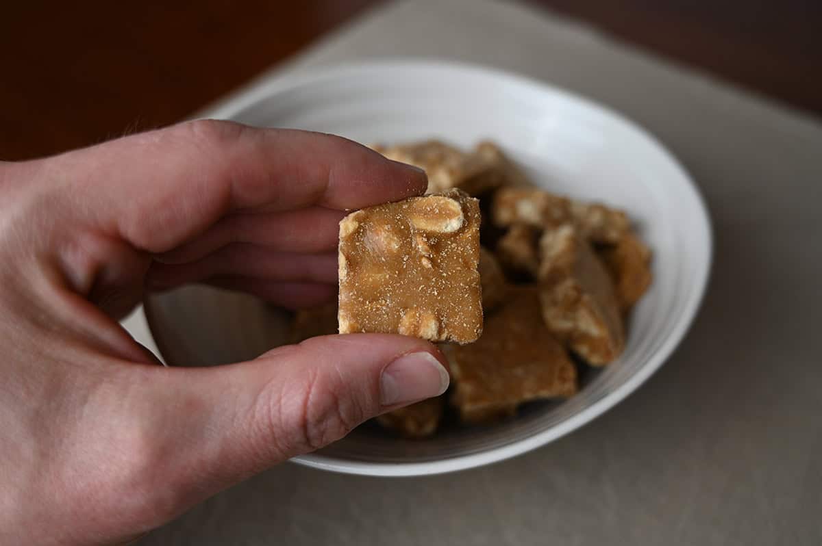 Image of a hand holding one peanut brittle bite close to the camera.