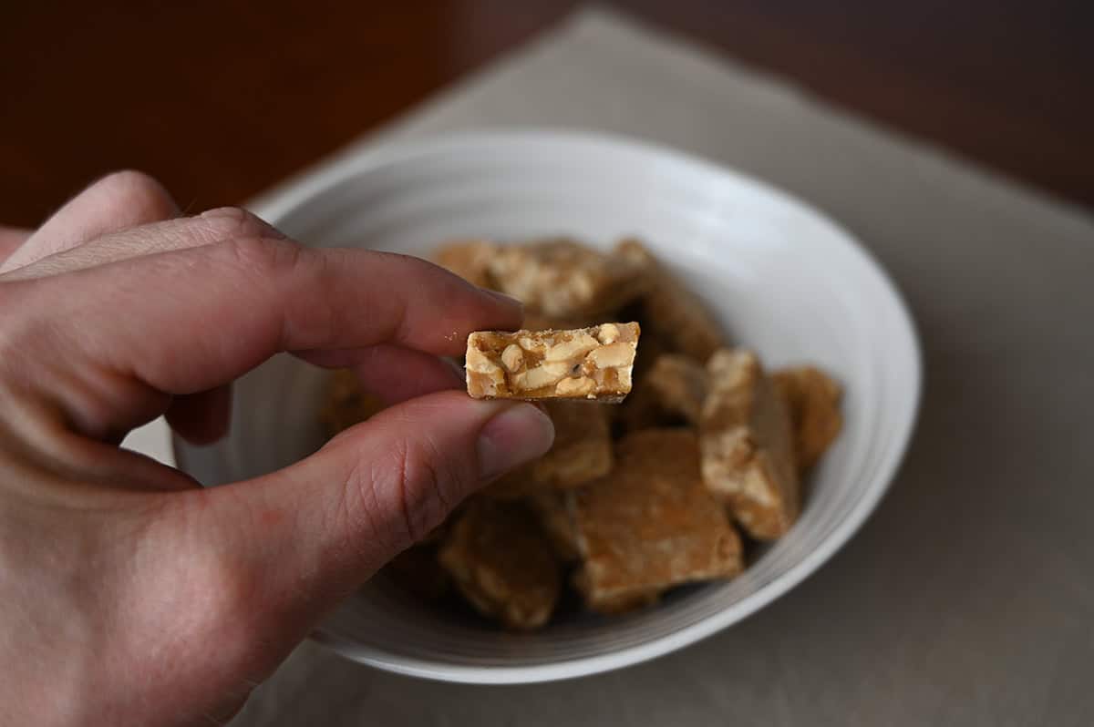 Image of a hand holding one peanut brittle bite close to the camera with a bite taken out of so you can see the center.