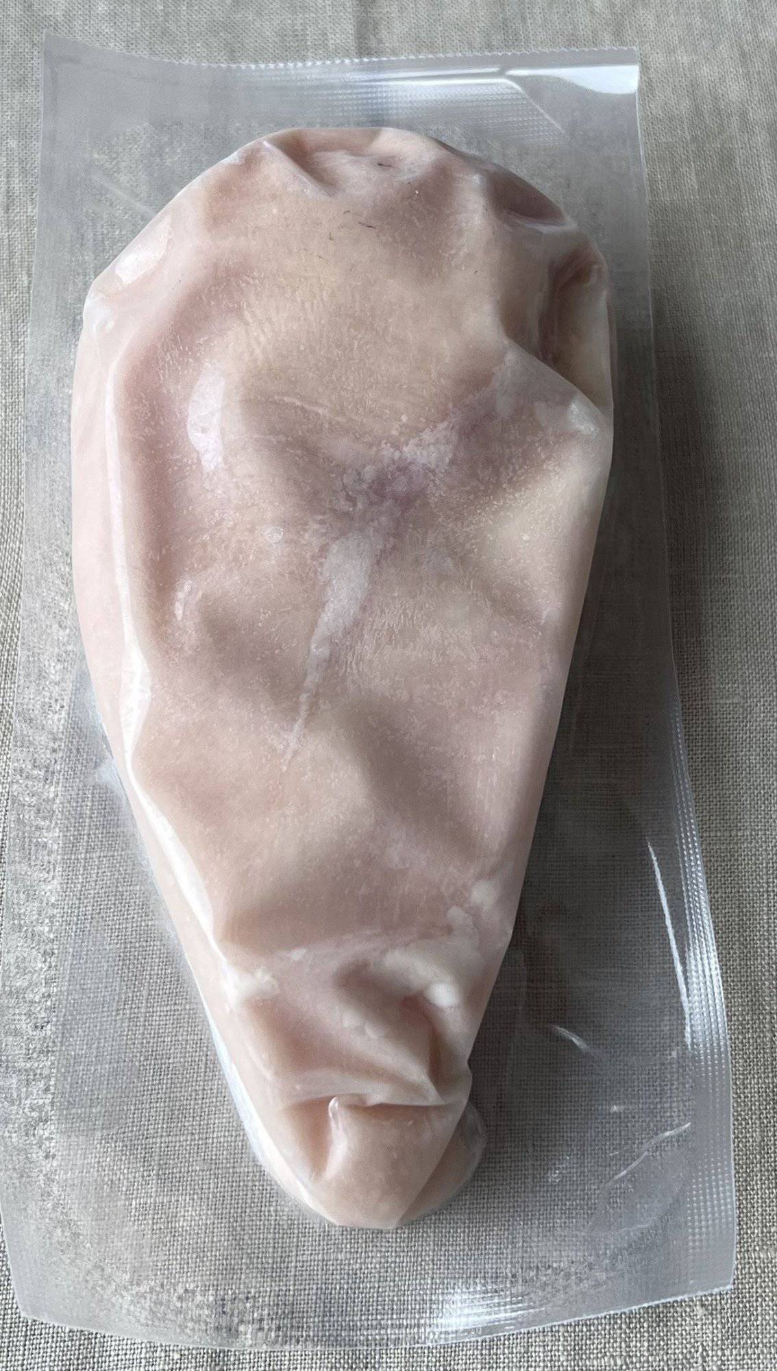 Image of one large individually vacuum sealed raw chicken breast sitting on a table.