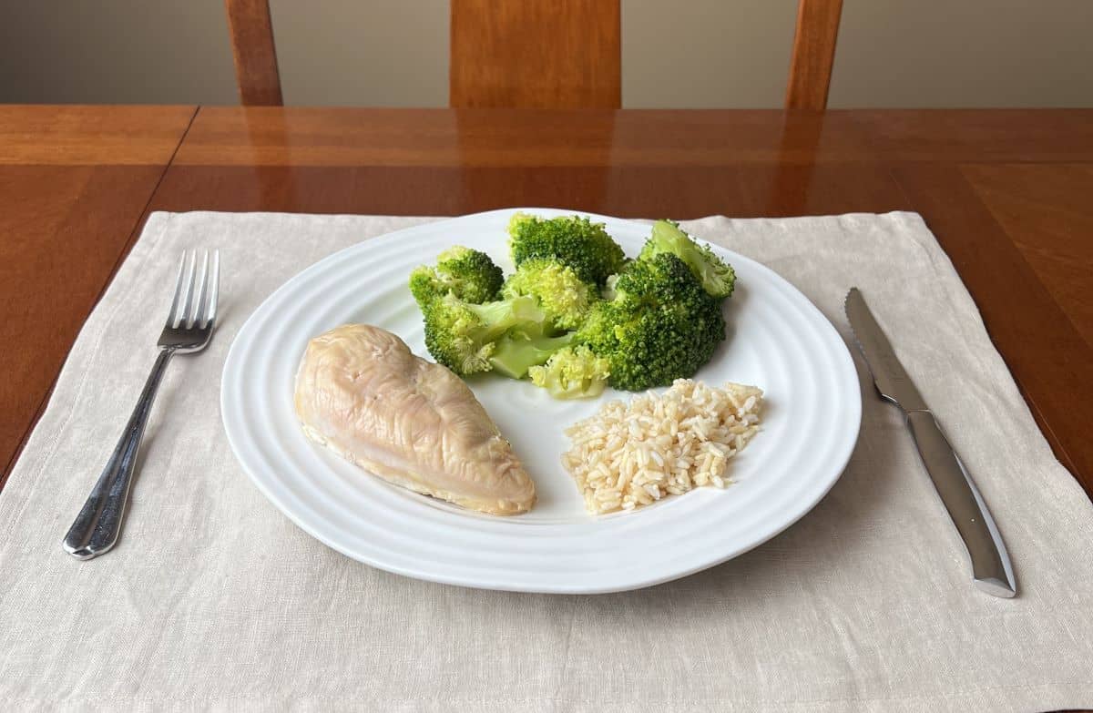 Image of a white plate with one chicken breast, rice and steamed broccoli served on it.