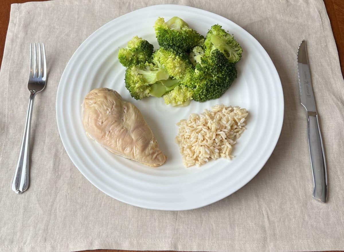 Image of a white plate with one chicken breast, rice and steamed broccoli served on it.