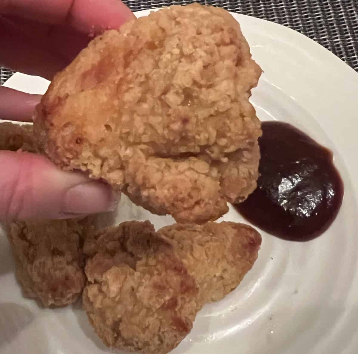 Image of a hand holding one crispy chicken wing close to the camera.