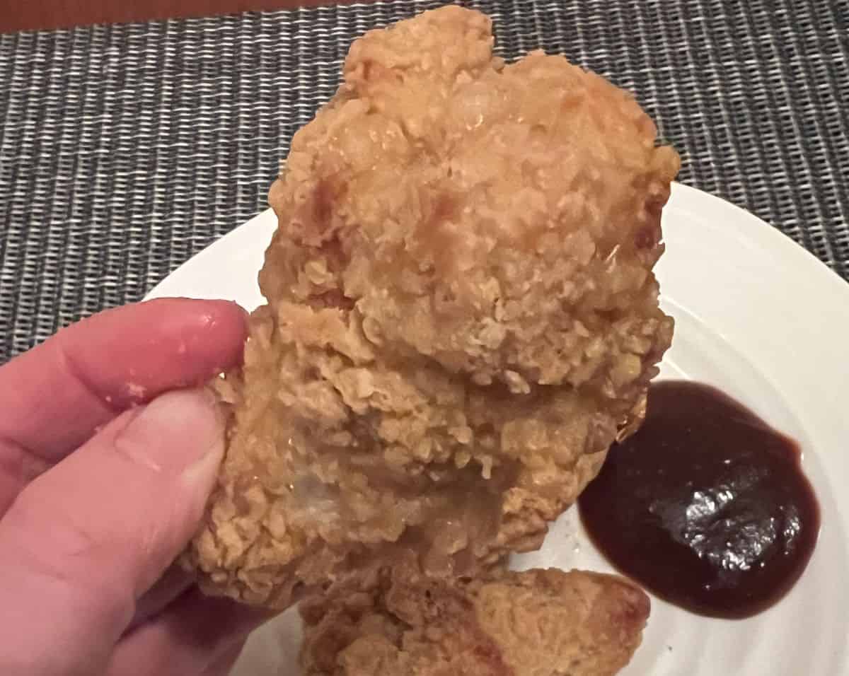 Close up image of a hand holding a chicken drumstick close to the camera with a plate of wings in the background. 