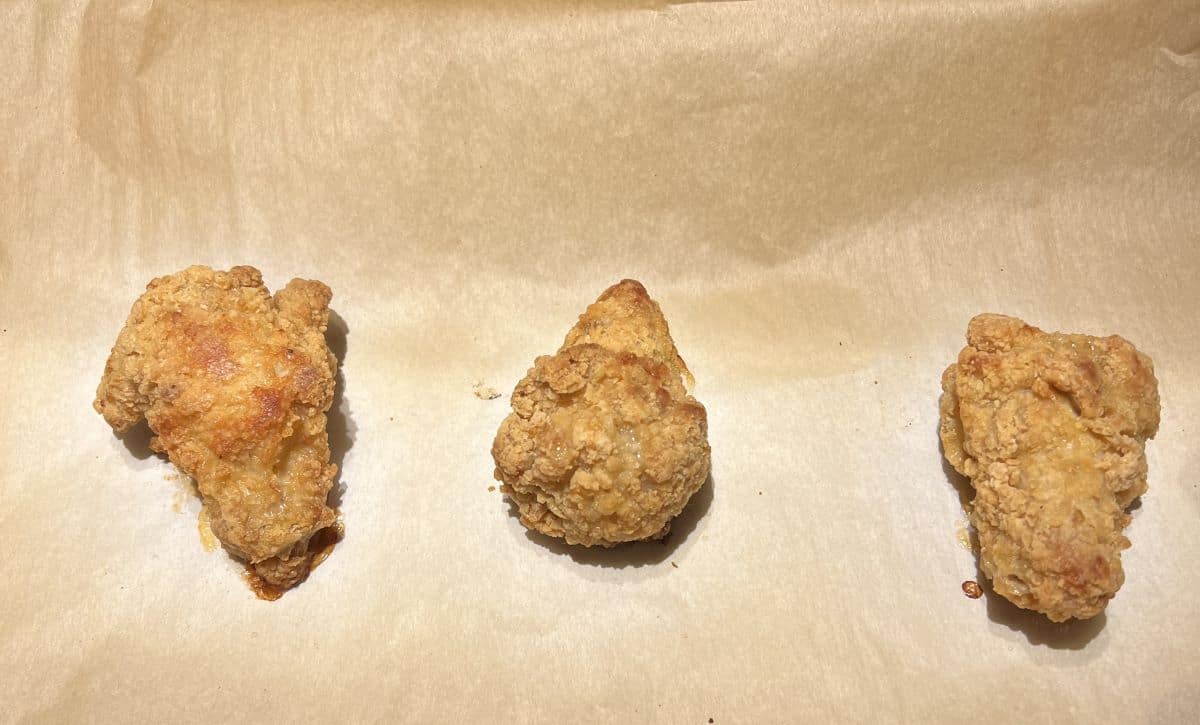 Image of three chicken wings sitting on a parchment lined cookie sheet after being cooked in the oven.