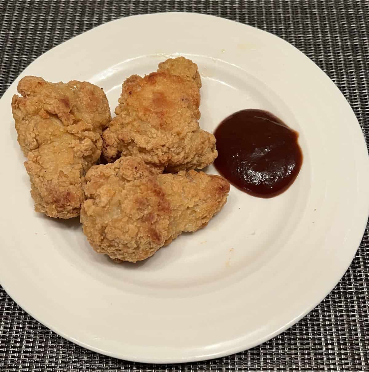 Image of three cooked chicken wings served on a white plate beside barbecue sauce.