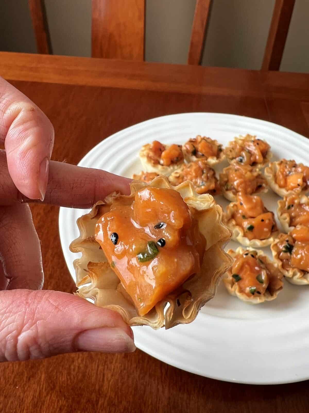 Closeup image of a hand holding one phyllo pastry shell with salmon poke in the shell. 