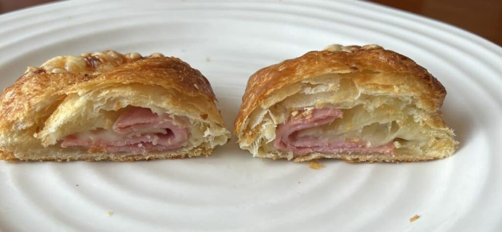 Image of one smoked ham & Swiss cheese pocket cut in half so you can see the inside of the pocket, served on a white plate. 