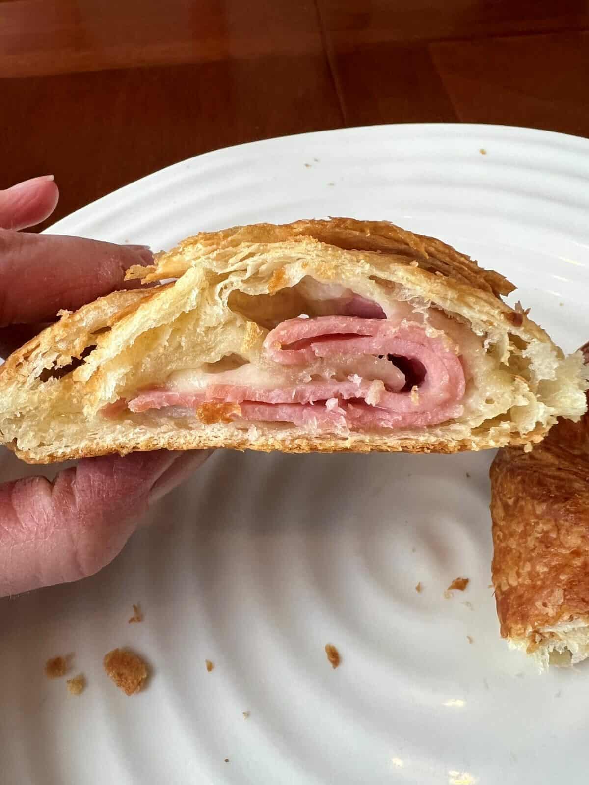 Image of a hand holding one half of a smoked ham & Swiss cheese pocket cut in half so you can see the ham and cheese in the pocket. 