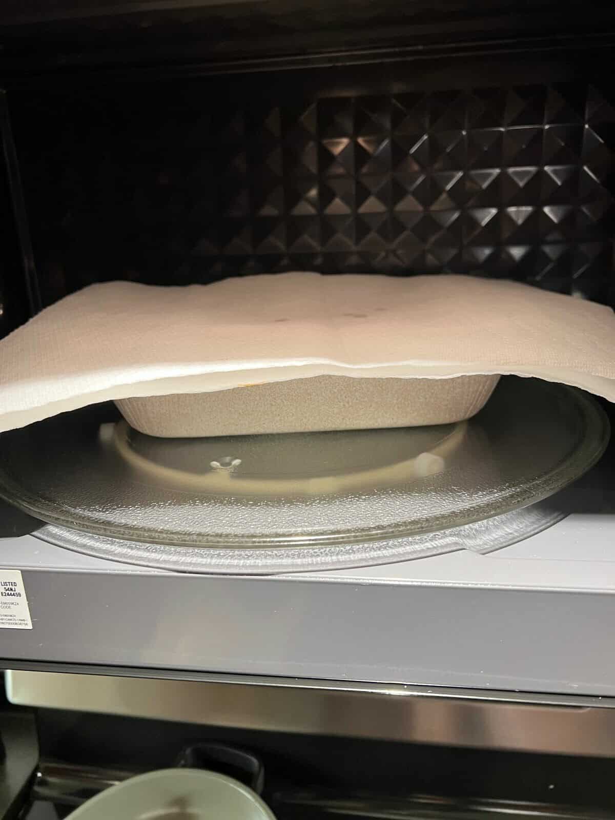 Image of the tray of pasta covered with paper towel sitting in a microwave. 