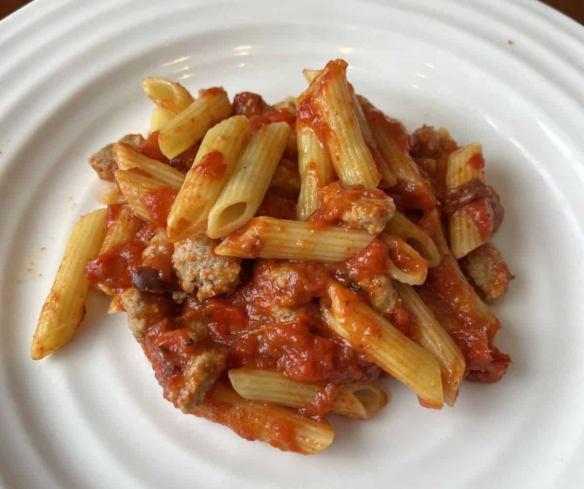 Top down image of a plate of penne with Italian sausage and red tomato sauce.