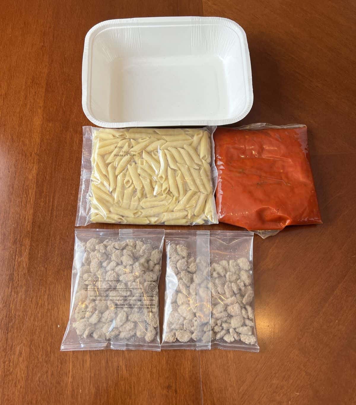 Image of the package contents, sauce, pasta and italian sausage sitting on a table unopened. 