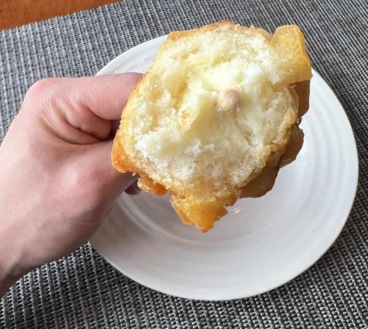 Image of a hand holding a crispy potato corn dog with a few bites taken so you can see the center.