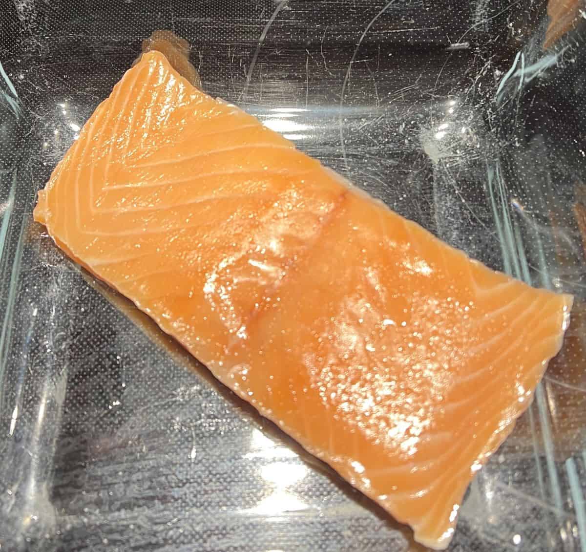 Closeup image of a raw piece of salmon sitting in a baking dish.