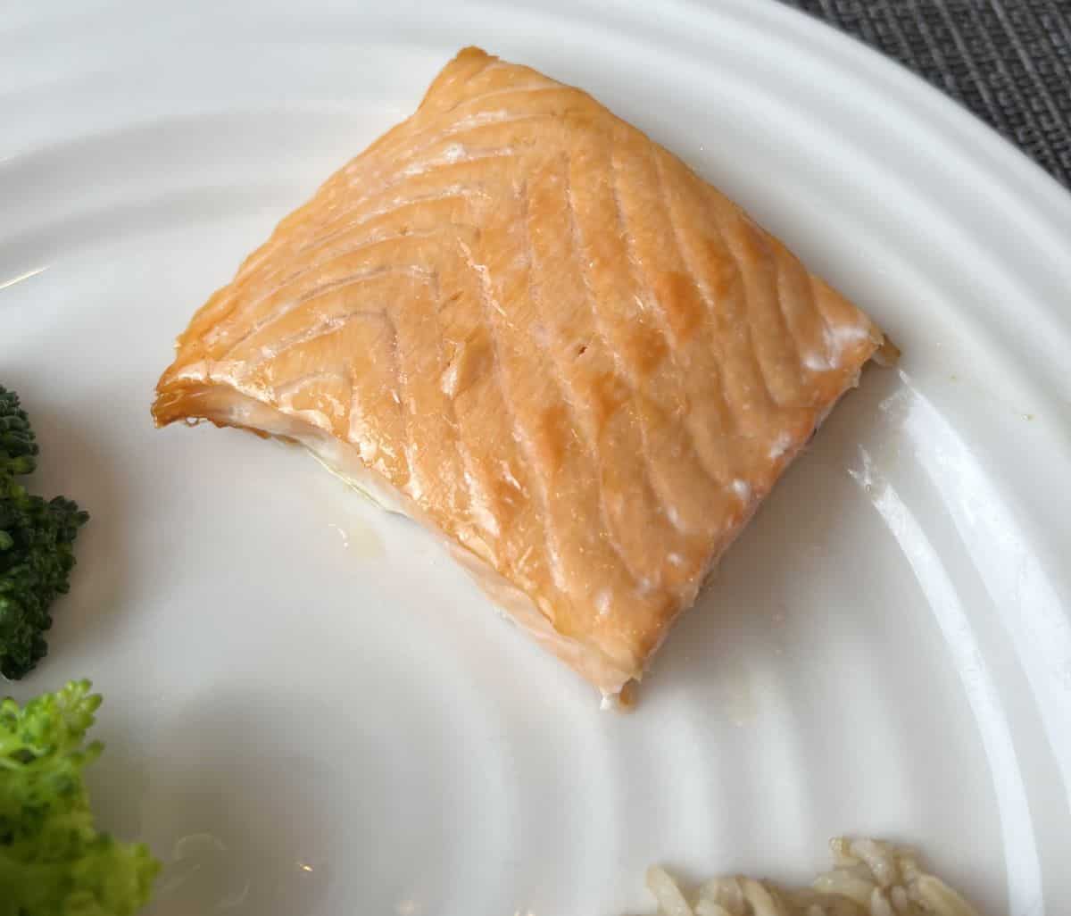 Closeup image of a piece of cooked salmon on a white plate.