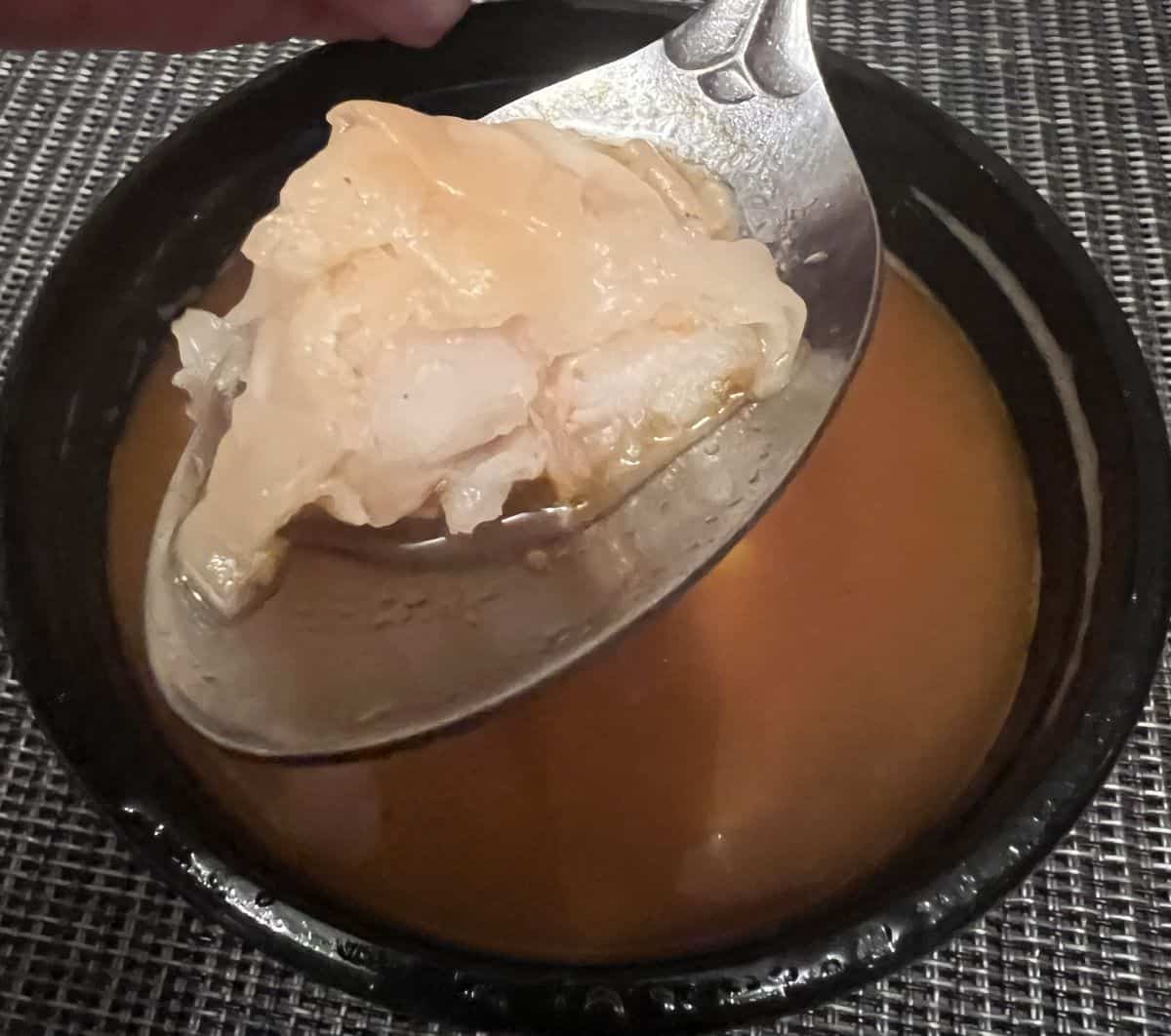 Closeup image of a spoon with a shrimp wonton on it hovering over a bowl of tom yum broth.