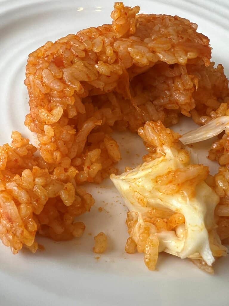 Image of the rice ball cooked and served on a white plate showing a cheese ball and a hollow rice cake sitting on the plate. 