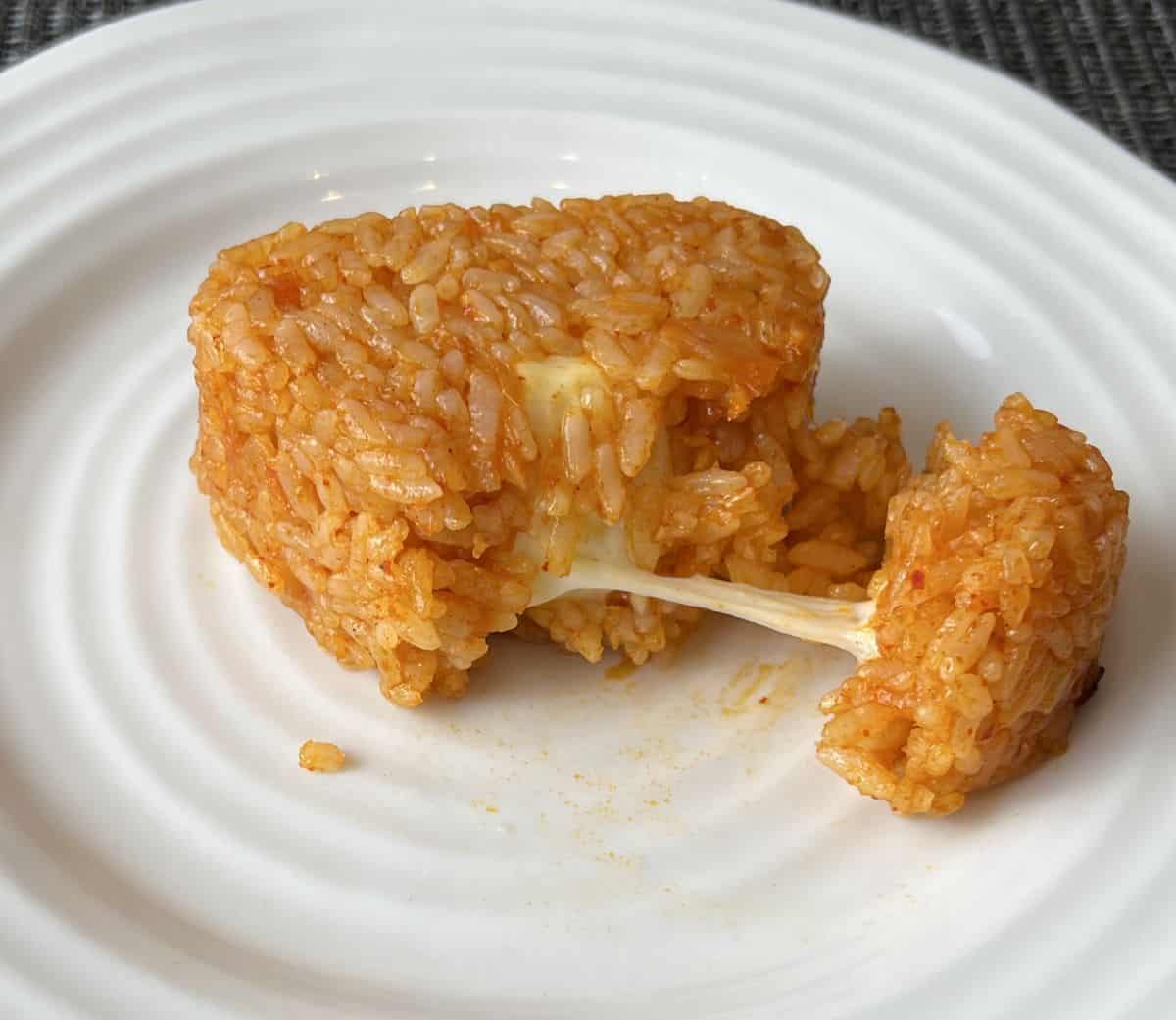 Closeup image of the rice ball served on a white plate cut in half so you can see the cheese in the middle. 