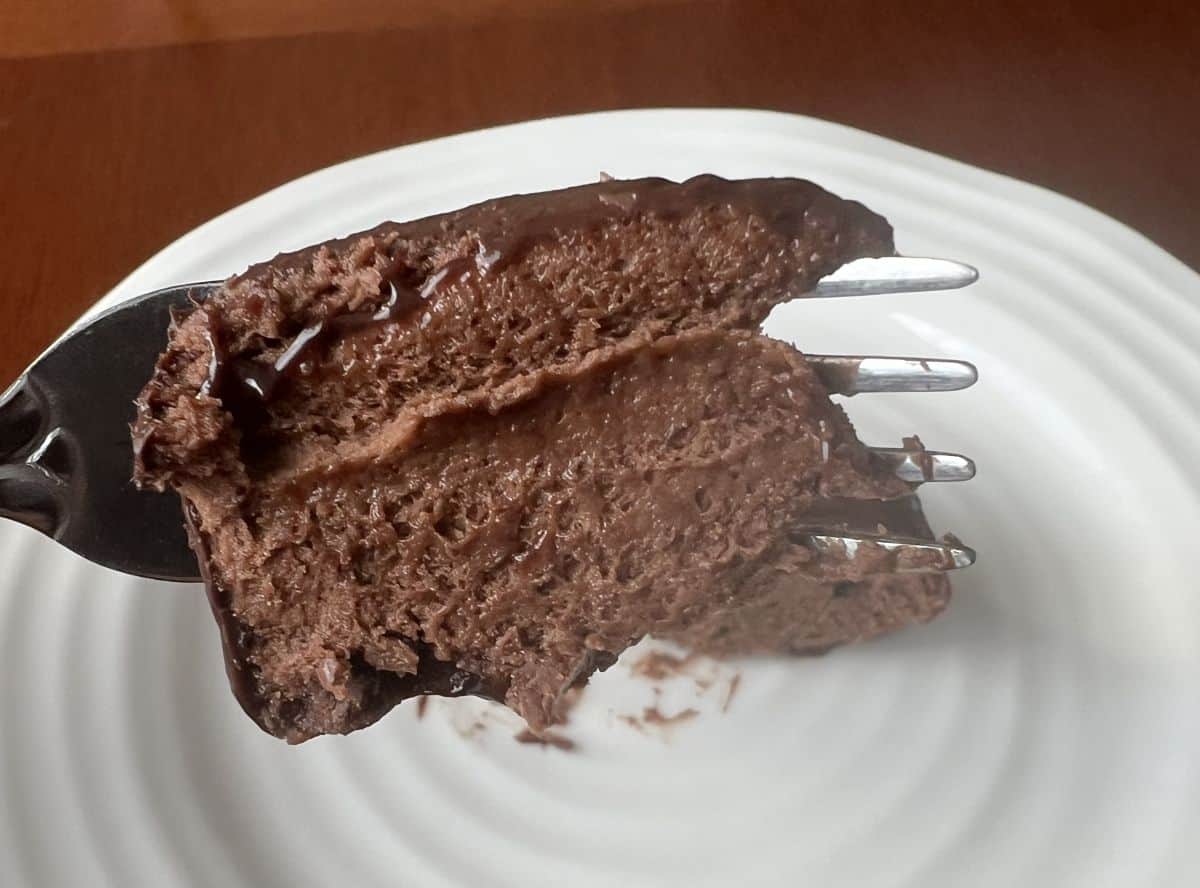 Closeup image of a fork with a bite of the chocolate mousse dessert on it hovering over a white plate.