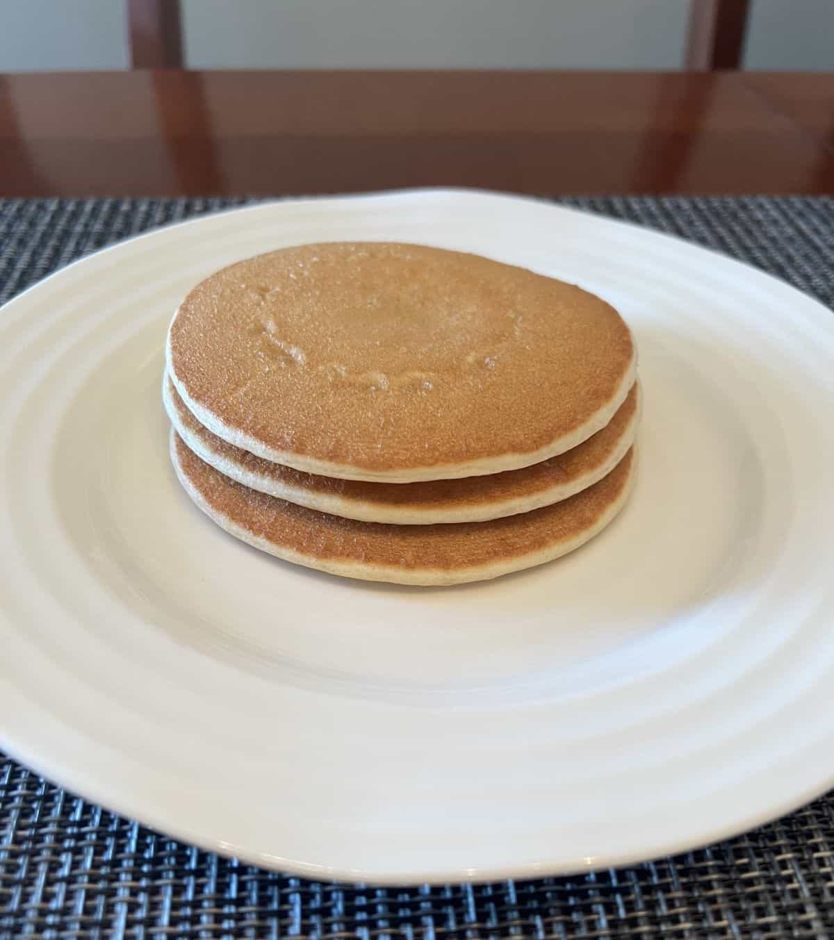 Image of a stack of three heated pancakes sitting on a plate.