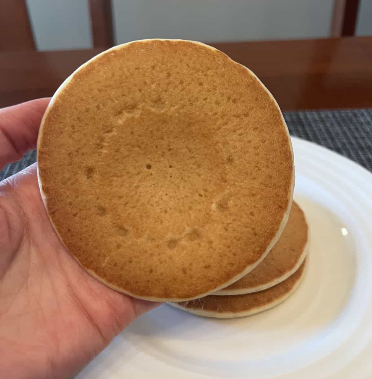 Closeup image of a hand holding one heated pancake close to the camera.